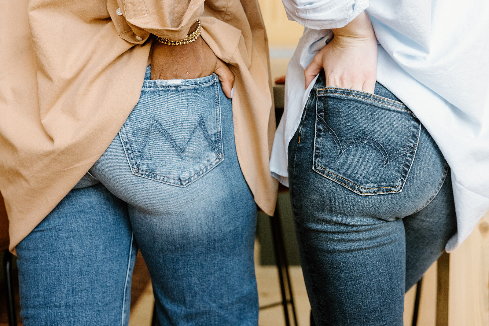 Two people standing close together, each with a hand in their respective denim back pockets.