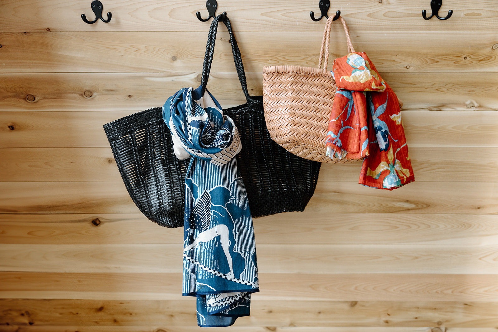 Beach bags and a scarf hanging on hooks against a wooden wall.