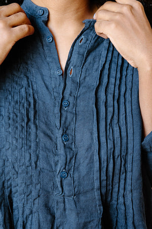 Close-up of a person adjusting a navy blue pleated shirt with buttons.