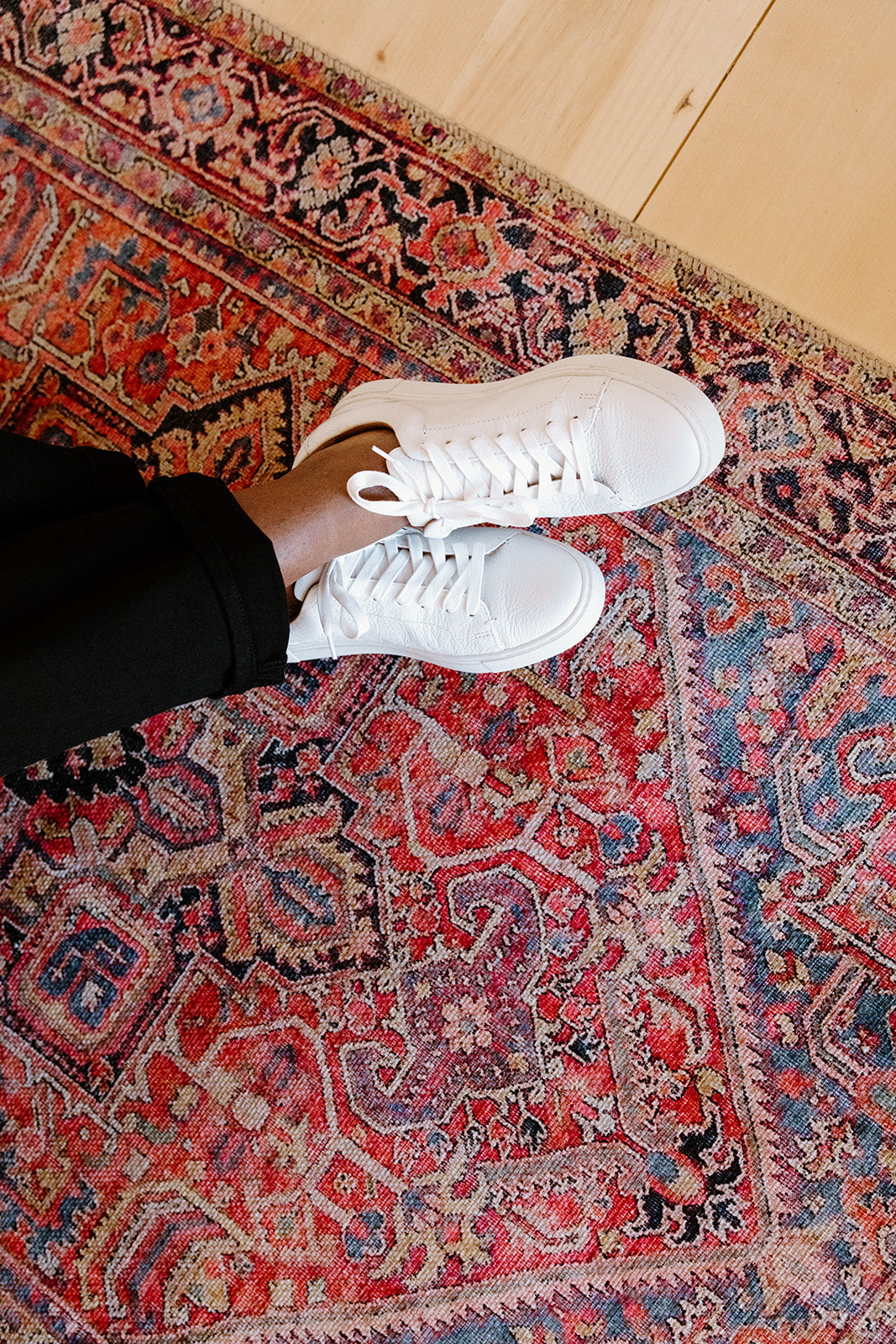 A person standing on a colorful rug wearing white sneakers and black pants.