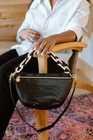 Woman sitting on a wooden chair with a black handbag.