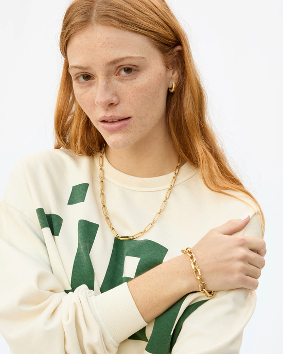 Woman with red hair wearing a cream sweatshirt with green lettering and 14k gold plated jewelry featuring a Clare V. Book Chain Necklace - 18in in Vintage Gold with lobster claw closure.