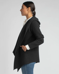 Profile view of a woman in a Margaret O'Leary St. Claire in Black cashmere cardigan over a white shirt, paired with blue jeans.