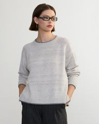 A woman with short brown hair and rectangular glasses wears the Margaret O'Leary Mendocino Pullover in Fog Combo, standing against a plain light background with her hands in her pockets, looking to the side.