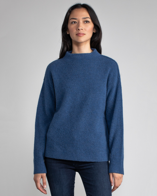 A woman wearing a Margaret O'Leary Charlotte Pullover in Sapphire and jeans stands against a neutral background.