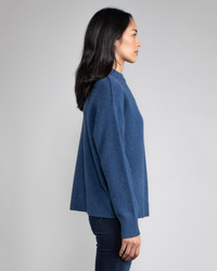 Woman in profile wearing a Margaret O'Leary Charlotte Pullover in Sapphire and jeans against a gray background.