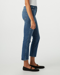 Side view of a person wearing AMO's Chloe Crop in Crush high rise jeans and black flats standing against a white background.