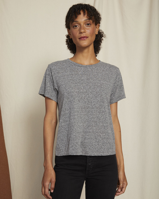Woman in an AMO Classic Tee in Heather Grey and black pants standing against a neutral background.