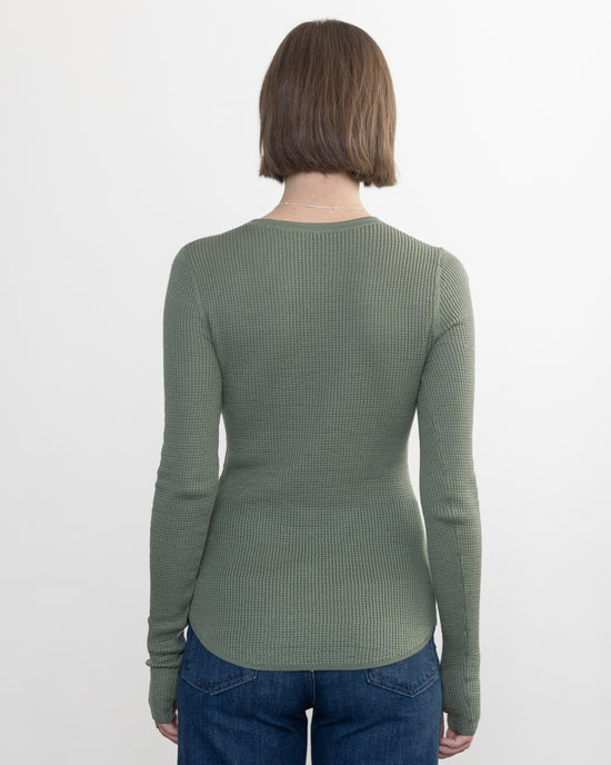 A person with short brown hair, wearing the Margaret OLeary Shirtail Waffle Crew in Sage and blue jeans, stands facing away against a plain white background.