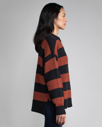 A person in a Margaret O'Leary Chelsea Pullover in Spice Stripe with relaxed fit and jeans standing in profile against a grey background.