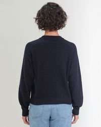 Person standing with their back to the camera, wearing a Margaret O'Leary Lola Pullover in Navy and blue jeans.