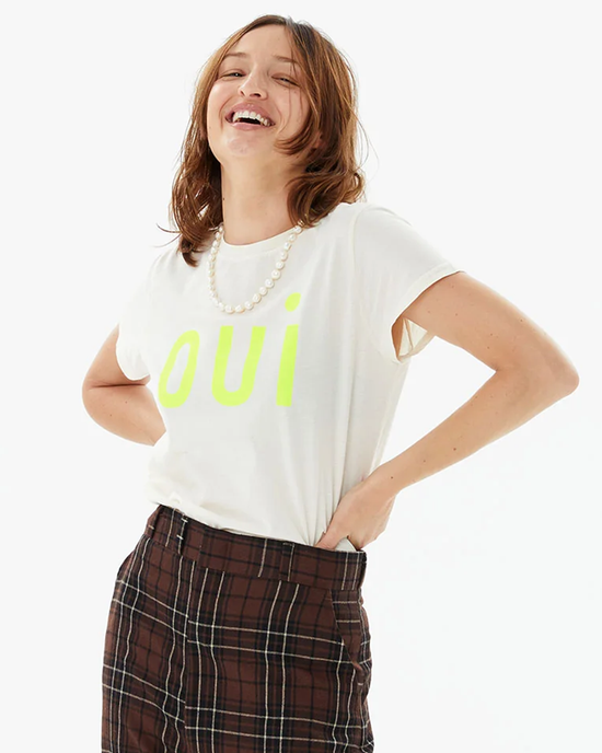 Woman smiling in a casual, lightweight, 100% cotton Clare V Oui Classic Tee in Cream w/ Neon Yellow, paired with checkered trousers.