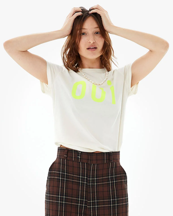 Woman in a lightweight, white Clare V Oui Classic Tee in Cream w/ Neon Yellow, holding her hands on her head, with a perplexed expression.