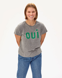 Woman smiling in a lightweight Clare V Oui Classic Tee in Grey w/ Fern, paired with blue jeans against a white background.