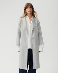 A woman in an American Vintage Dadou Love Coat in Polaire over a white blouse and dark trousers stands against a neutral background.