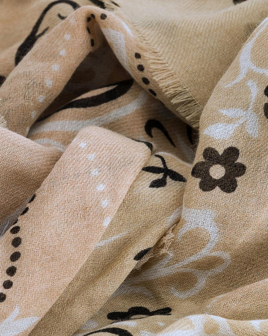 Close-up of the Classic Wool & Silk Bandana in Beige by Maison Lecomte Flament, featuring black and white floral and dot patterns on slightly textured, wrinkled wool-silk fabric with frayed edges.