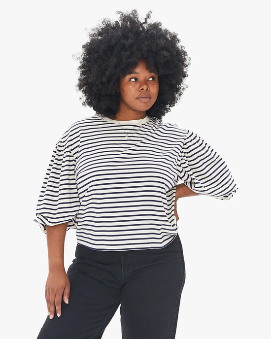 A woman with curly hair wearing a Clare V. Drop Shoulder Tee in Navy & Cream Stripe and black High Rise Straight Leg Denim stands confidently with one hand on her hip.