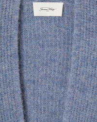 Close-up of a blue woolen fabric with an "East Cuffed Sleeve Cardi in Ouragan Chine" label on an open shaker knit by American Vintage.