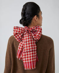 A woman with dark braided hair, seen from behind, wears a brown sweater and a large Moismont Vichy Wool Scarf No 693 in Flowers Lipstick, tied in a bow at the back of her neck.