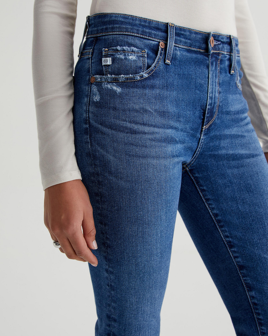 Close-up of a person wearing blue Prima in Brighton mid-rise jeans by AG Jeans with a hand resting on the hip.