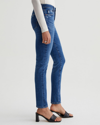 Side view of a person wearing blue AG Jeans Empower Denim mid-rise jeans and black open-toe heels.