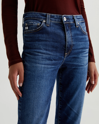 Close-up of a person wearing AG Jeans' Mari in 8Ys East Coast high-rise straight leg blue jeans with a focus on the upper part of the jeans and a maroon top.