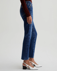 Side view of a person wearing AG Jeans Mari in 8Ys East Coast high-rise straight leg blue jeans and white heeled shoes.