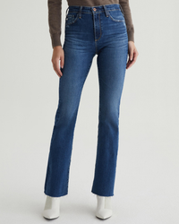 Woman wearing high-rise, bootcut jeans with a raw hem and white boots, including the Farrah Boot in Brighton by AG Jeans.
