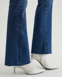 High-rise flared blue Farrah Boot in Brighton jeans with raw hem paired with white pointed-toe heels from AG Jeans.