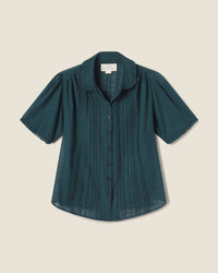 The Millie Blouse in Sea Pine Check by Trovata Birds of Paradis features short sleeves, a button-up front, rounded collar, and gathered shoulders in dark green and navy plaid, shown on a light beige background.