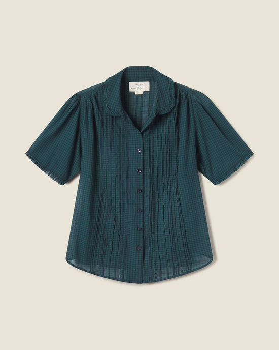 The Millie Blouse in Sea Pine Check by Trovata Birds of Paradis features short sleeves, a button-up front, rounded collar, and gathered shoulders in dark green and navy plaid, shown on a light beige background.