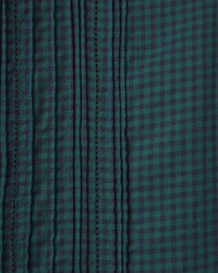 Close-up of the Blair Dress in Sea Pine Check by Trovata Birds of Paradis shows vertical stitched pleats on the left for texture and a smooth checkered pattern on the right, highlighting the tiered midi skirt’s distinctive design.