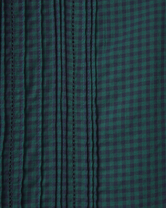 Close-up of the Blair Dress in Sea Pine Check by Trovata Birds of Paradis shows vertical stitched pleats on the left for texture and a smooth checkered pattern on the right, highlighting the tiered midi skirt’s distinctive design.