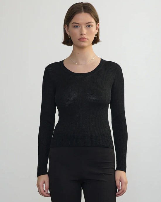 A woman with short brown hair wears the Margaret OLeary Scoop Neck Pullover in Black and black pants, standing against a plain light gray background and looking directly at the camera with a neutral expression.
