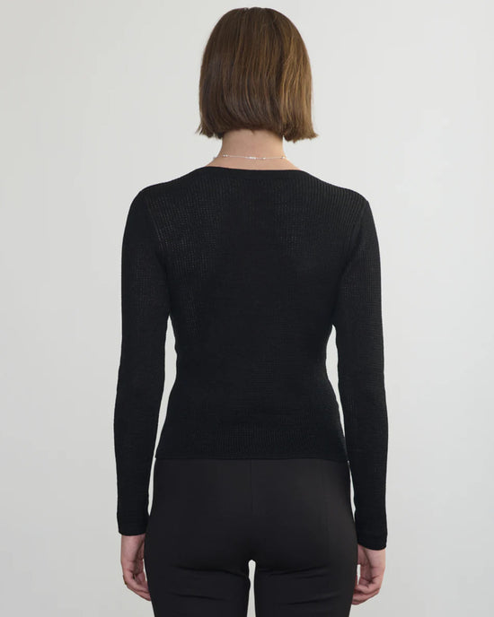 A person with short brown hair is seen from behind, wearing the Margaret OLeary Scoop Neck Pullover in Black and black pants, standing against a plain light background.