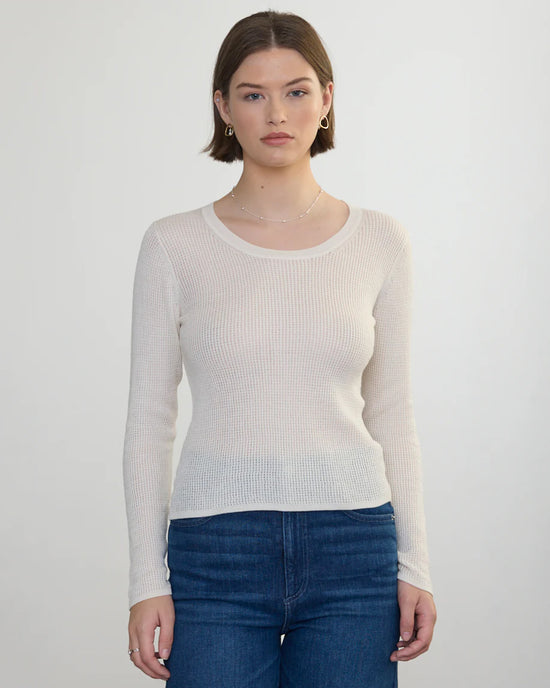 A woman with short brown hair wears a Margaret OLeary Scoop Neck Pullover in Ivory and blue jeans, standing facing the camera against a plain light background.