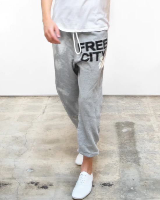 Person standing in Bleachout Superfluff OG Sweatpant in Heather Bleachout with the words "FREECITY" on one leg and white sneakers, part of a matching set.
