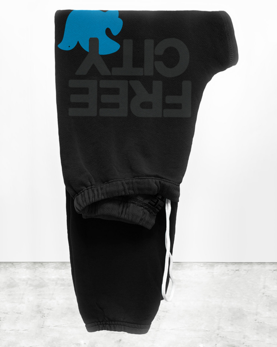 Black Free City French Terry sweatpants with the logo "oliver tree" folded and hanging on a wall.