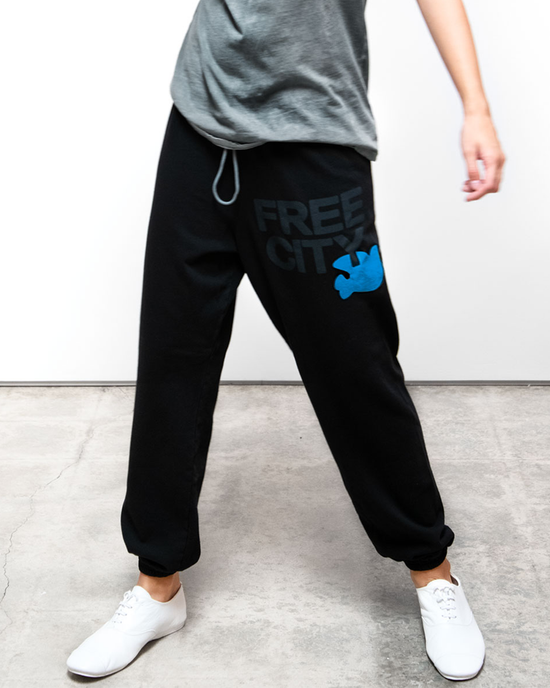Person wearing black Free City French Terry sweatpants with "FREECITY" logo and white sneakers standing against a white background.