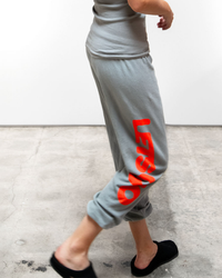 Woman in grey 100% cotton Lets Go OG Supervintage sweatpants with red "Free City" logo walking on concrete floor, wearing black slippers, partial torso visible.