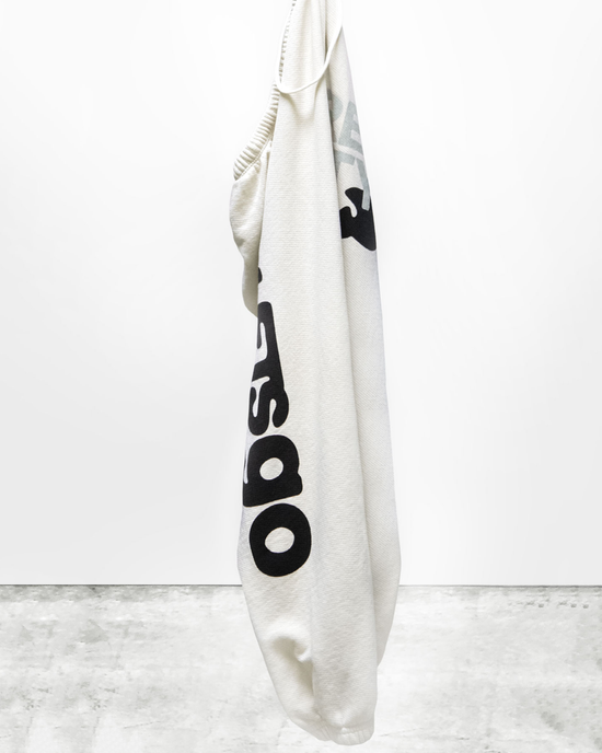 A white sweatshirt with black lettering, part of a matching set, hanging on a hook against a white wall from Free City.