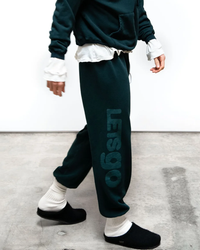 Person in casual Free City SY OG Freecityletsgo Sweatpant in Green Plant attire with the phrase "let's go" printed on the side of their pants.