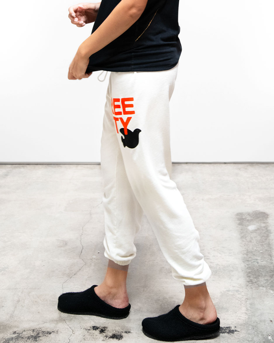 Person in white Free City Large Sweatpants in Creamy Yum with a graphic design standing against a plain background.