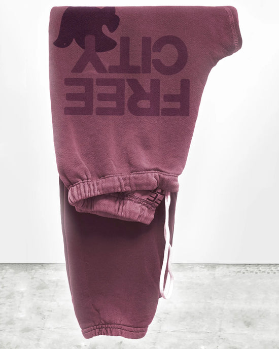 The FC Large Sweatpant in Roses by Free City features maroon French Terry fabric, a drawstring waist, and FREE CITY with a bird silhouette on the upper thigh. Folded presentation, minimalistic background. Made in USA.