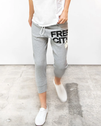 Person wearing Large 3/4 Sweats in Heather Cream with "FREECITY" print and white sneakers walking on a concrete surface.