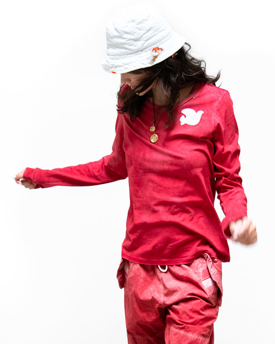 Woman in a Free City LNLSun Longsleeve T in Artyard Red Glass outfit with a white bucket hat, looking down.