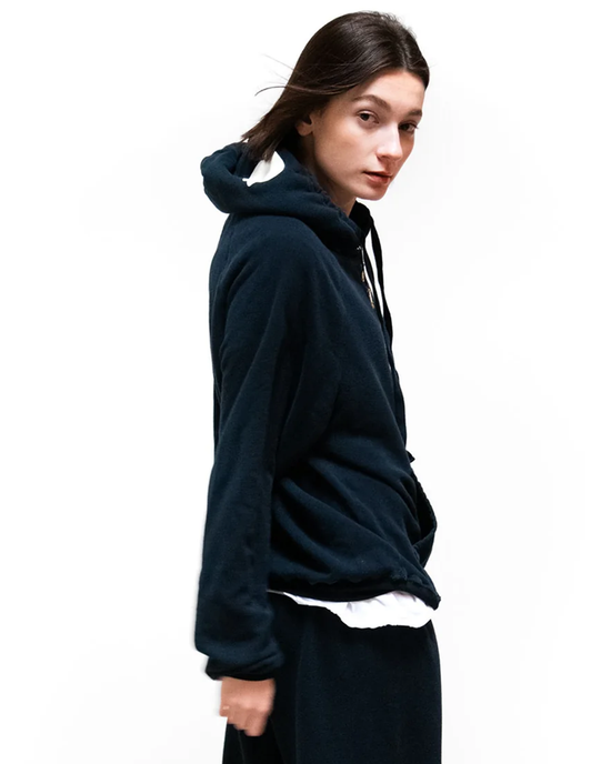 Woman in a navy Free City SY Big Hoodie in Deepspace/Cream and dark skirt looking over her shoulder against a white background.