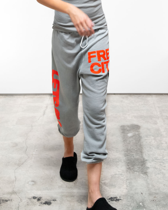 Person wearing Lets Go OG Supervintage Sweatpant in Silver Plant by Free City, standing in a plain room, paired with black slippers.