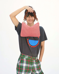 A person smiling while playfully holding a pink, handwoven Clare V Rattan Flat Clutch w/ Tabs in Petal over their head.