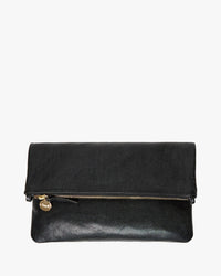 The Foldover Clutch w/ Tabs - Petit Caviar in Black by Clare V. is a black Italian leather clutch with a gold zipper and a small round gold charm on the pull, shown against a white background.